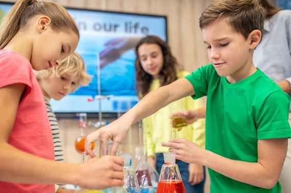 Practical work. Boy and girl standing sideways to camera with beaker and test tube doing chemistry experiment in class